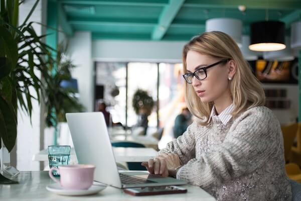 Concentrated female student preparing for exam in cafe. Busy young businesswoman using laptop to work. She reading business article. Lifestyle concept